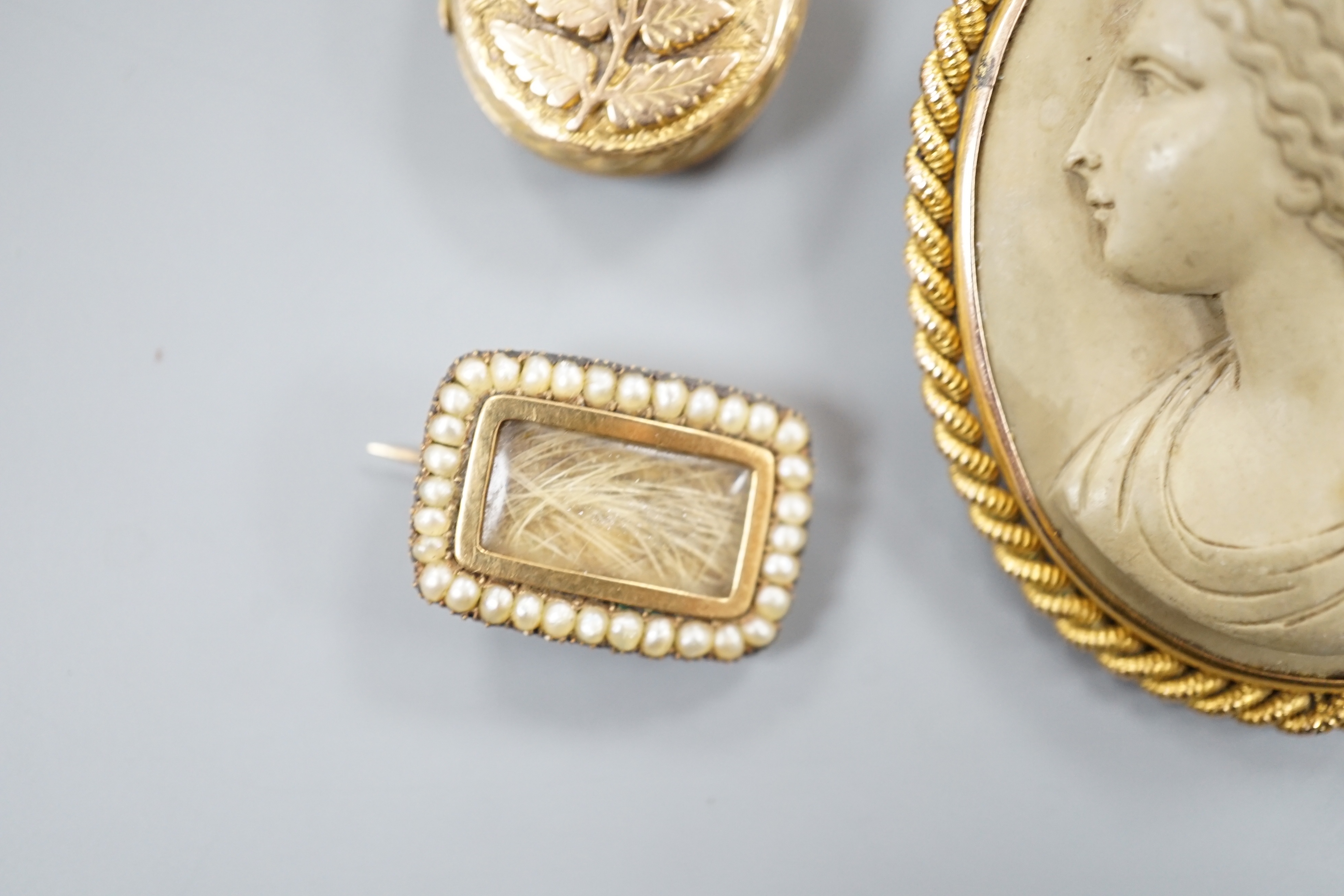 A 19th century yellow metal, seed pearl and plaited hair set mourning brooch, 20mm, a yellow metal oval locket and a mounted lava brooch.